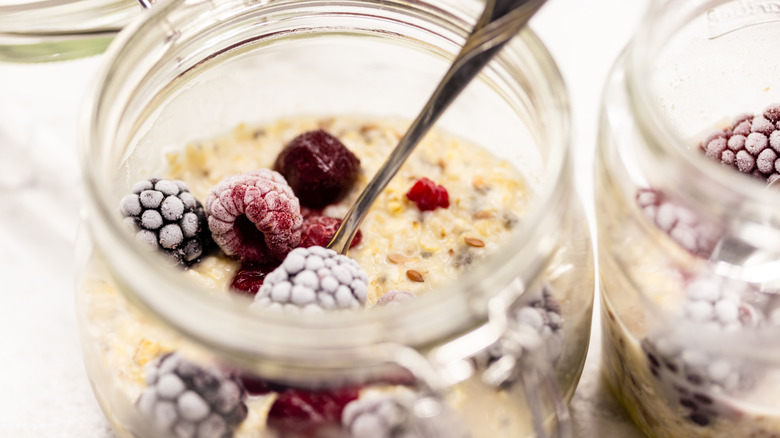 Two glass jars of overnight oats topped with frozen berries