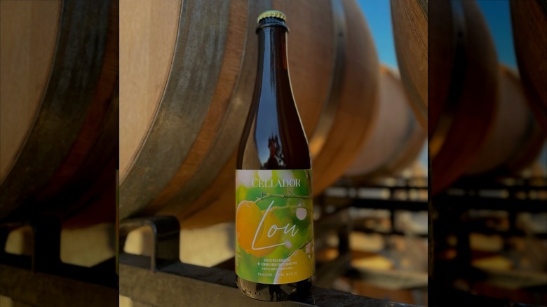 Bottle of Lou in front of oak barrels