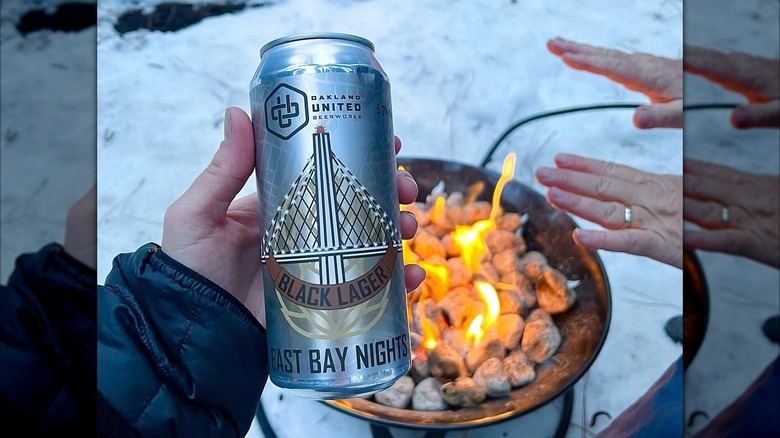 Hand holding a can of East Bay Nights over a fire