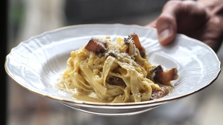 person holding out a plate of pasta with bacon