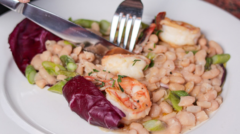 person cutting into shrimp and bean dish