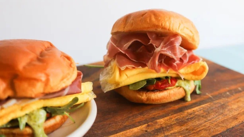 Pesto and prosciutto breakfast sandwiches on wooden cutting board
