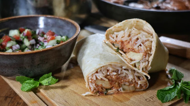Indian Butter Chicken Burrito on wooden board with salad and mint