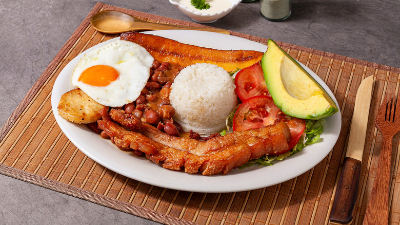 Plate of traditional Colombian bandeja paisa with rice, avocado, plantains, beans, and a fried egg