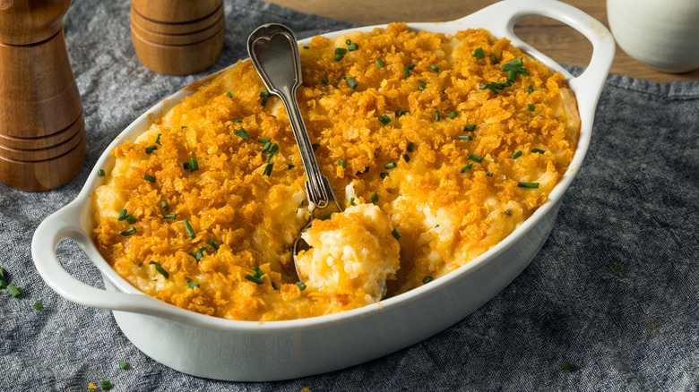 Cheesy funeral potatoes in white casserole dish with spoon