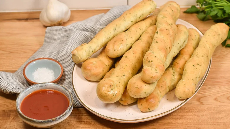 Homemade breadsticks with salt and marinara dip stacked on a plate