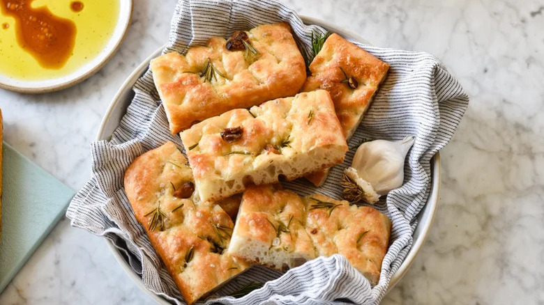 Pieces of focaccia on towel in a bowl with olive oil on the side