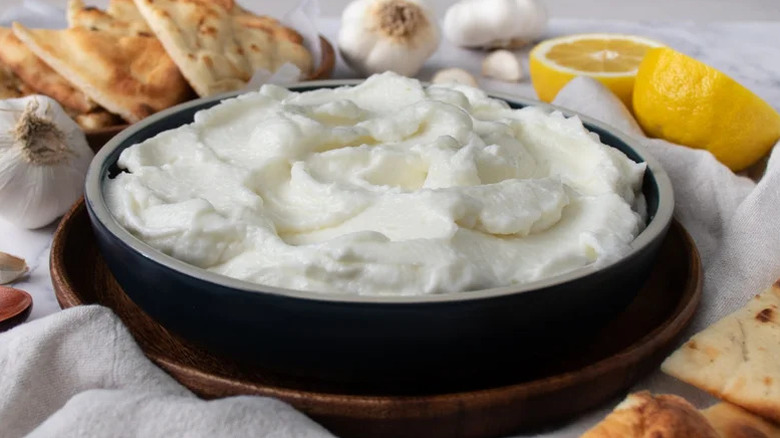 A bowl of toum with pita, lemon, and garlic on the side