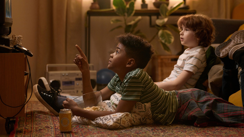 Picture of two kids on the floor eating snacks and watching TV.