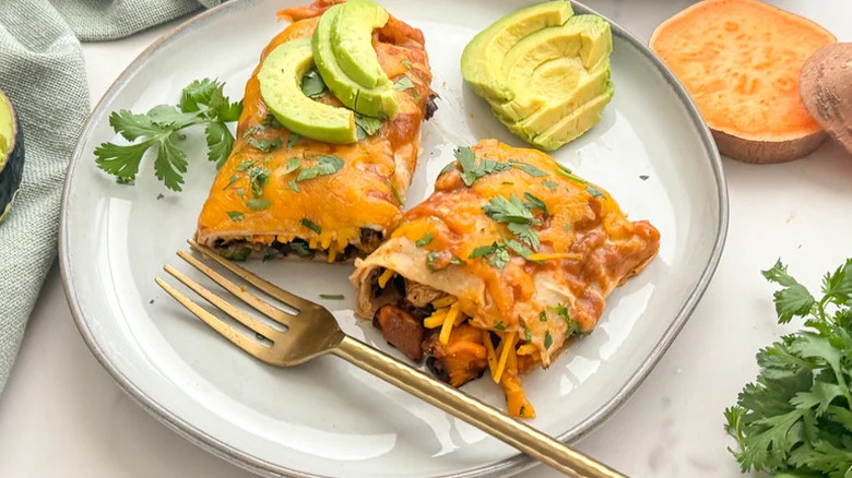 Roasted Vegetable and Black Bean Enchiladas on white plate with sliced avocado