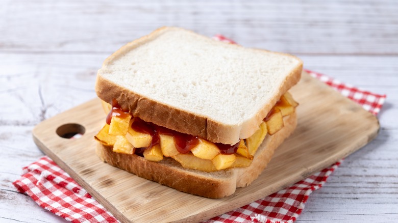 A chip butty shown on a chopping board that sits upon a folded tablecloth