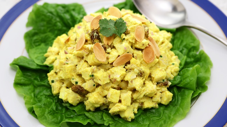 Coronation chicken shown on salad leaves with herbs and nuts sprinkled on the top