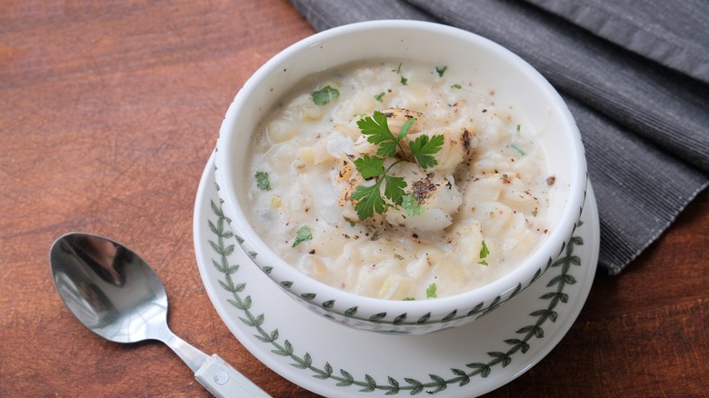 A bowl of cullen skink on a plate with a spoon laid on the side