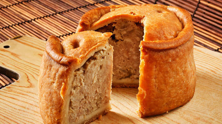 A large pork pie on a chopping board with a large piece cut out