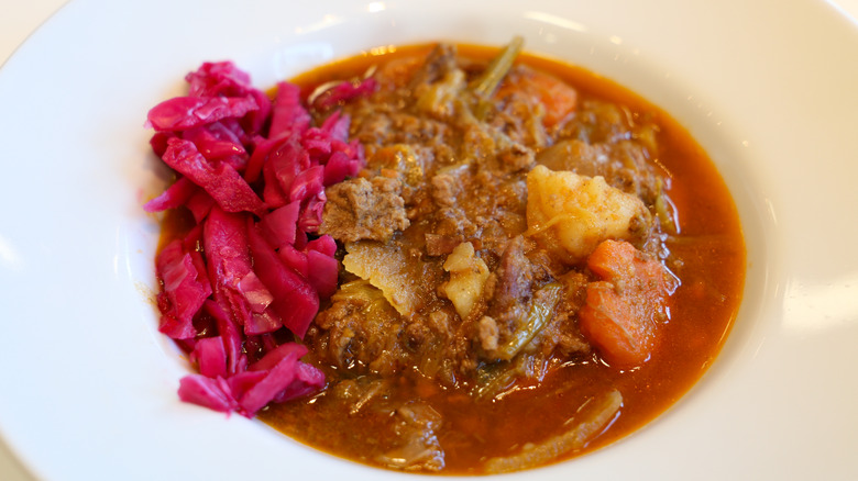 A closeup of a stew called scouse in a white bowl with pickled cabbage on the side