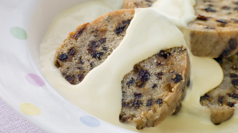 Sliced pieces of spotted dick in a bowl with custard poured over the top