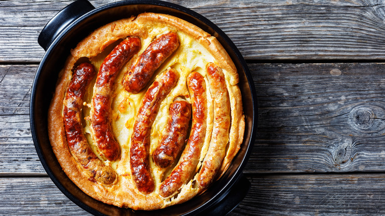 A dish full of cooked toad in the hole placed on a wooden background