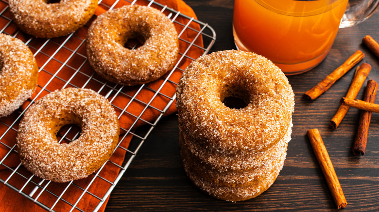 Apple cider donuts coated in sugar alongside cinnamon sticks and glass of cider on table