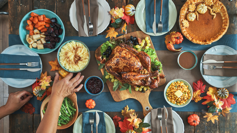 Hands laying various fall dishes on table, including corn, pumpkin pie, and turkey