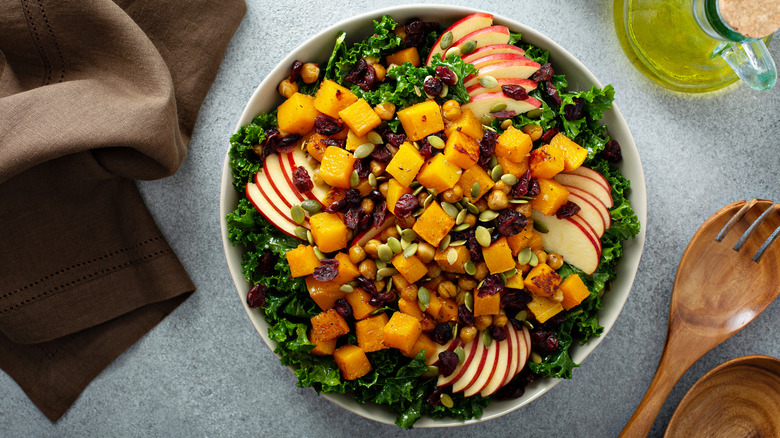 Overhead shot of kale salad topped with squash cubes, chickpeas, apple slices, and cranberries