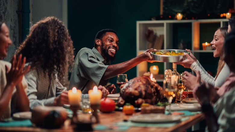 Friends passing food across Thanksgiving table
