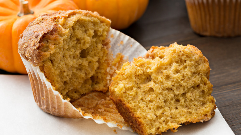 Pumpkin muffin broken in half to show soft interior, pumpkins in background