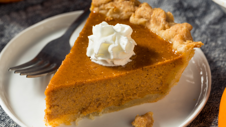 Slice of pumpkin pie topped with whipped cream on plate alongside fork