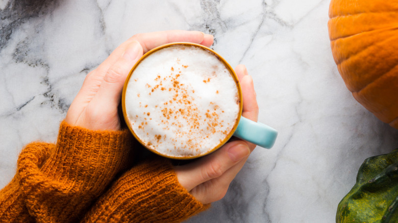 Overhead shot of hands cupping mug filled with pumpkin spice latte on granite countertop