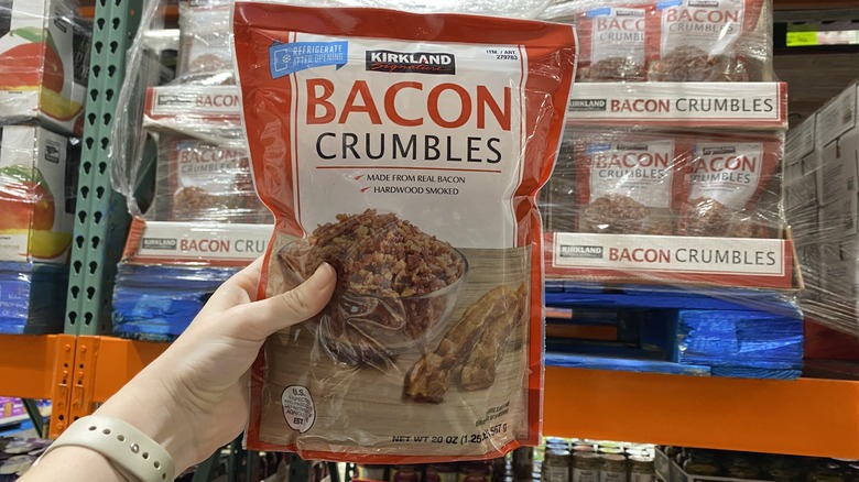 Hand holding up package of Kirkland brand bacon crumbles, with a photo of crumbled bacon sitting next to bacon strips on package
