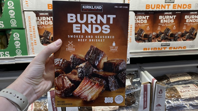 Hand holding up package of Kirkland Signature burnt ends in freezer aisle of Costco