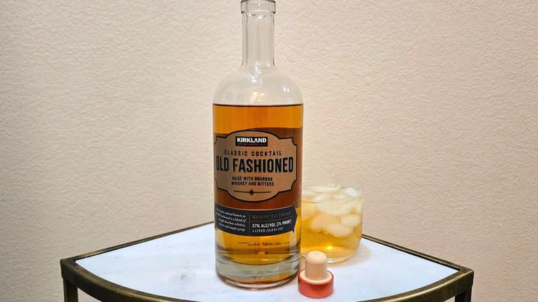 Bottle of Kirkland Signature pre-mixed Old Fashioned sitting on table next to golden-brown cocktail in glass of ice
