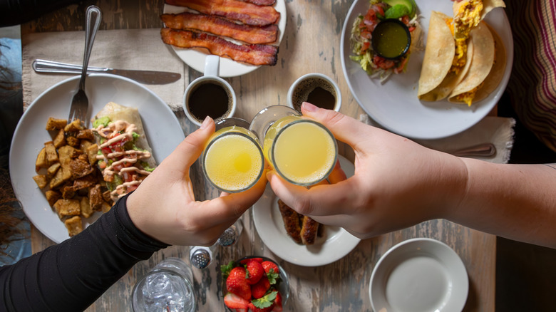 Two people toasting over brunch table with mimosas
