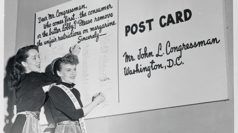 Two women signing an oversized postcard appealing margarine laws