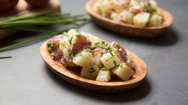 Potato salad on wooden serving plates, topped with fresh chives
