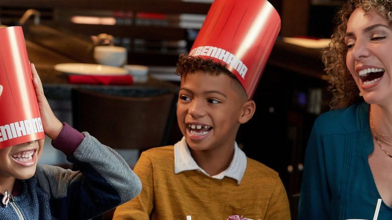 An adult and two children enjoying a celebration at Benihana while wearing imitation chef hats