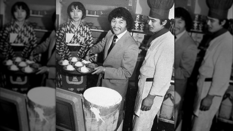 A shot of Hiroaki Aoki serving up food with two staff members