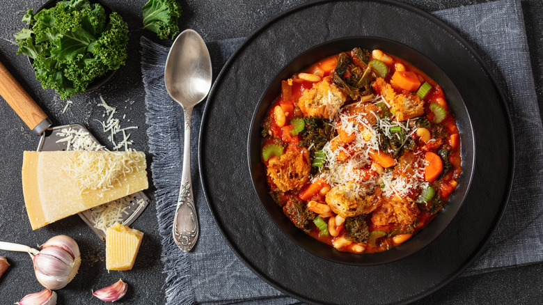 black bowl of Ribollita next to cheese, greens, and garlic