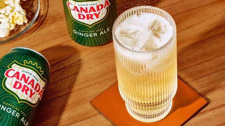 Glass of ginger ale on coaster surrounded by cans and popcorn