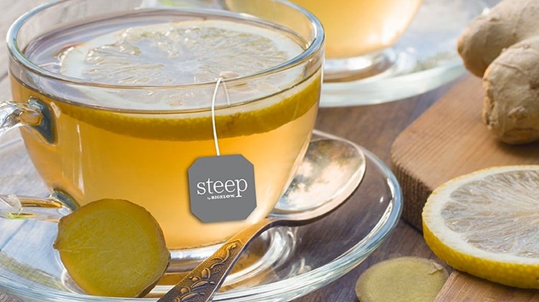 Glass cup of tea surrounded by lemon and ginger