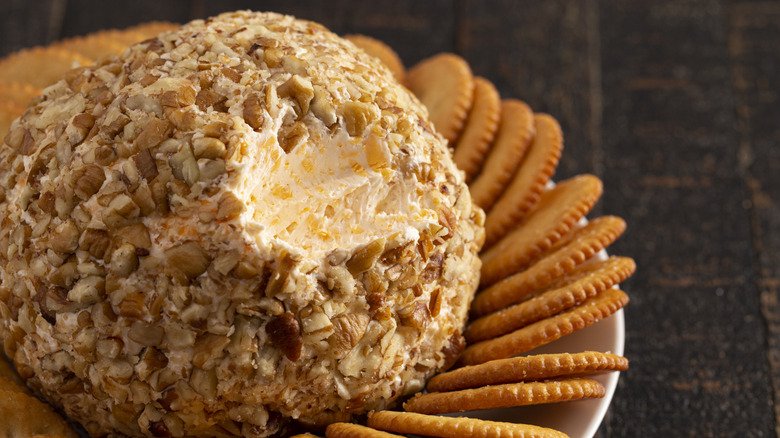 A cheese ball covered in chopped nuts with crackers on the side