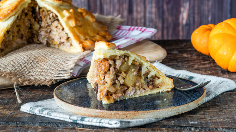 A slice of pork apple pie on a plate with the rest of the pie in the background