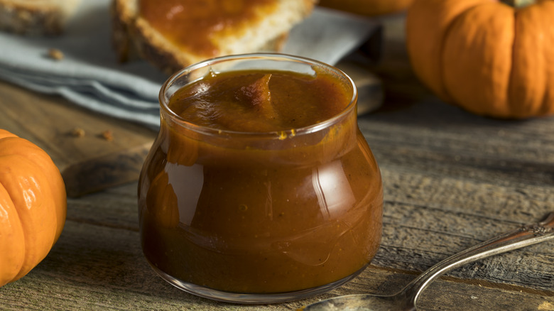 Pumpkin butter in a jar surrounded by small pumpkins