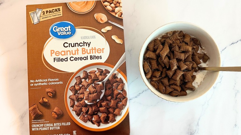 Box of Great Value Crunchy Peanut Butter Filled Cereal Bites cereal next to bowl of cereal with spoon on marble surface