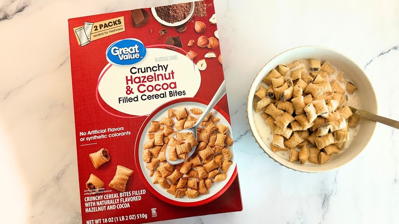 Box of Great Value Crunchy Hazelnut & Cocoa Filled Cereal Bites cereal next to bowl of cereal with spoon on marble surface