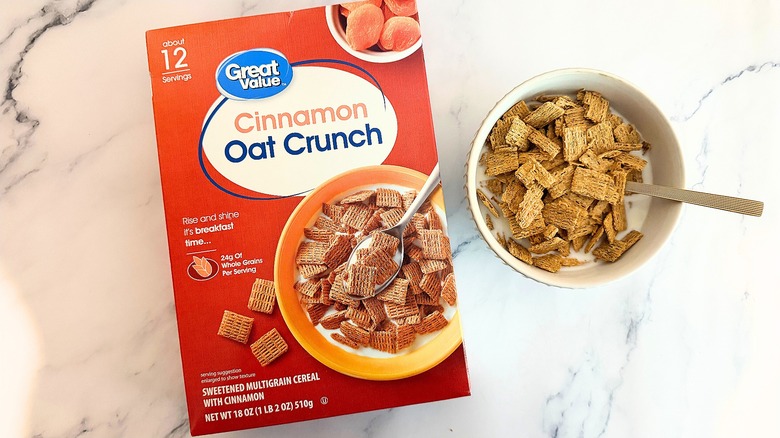 Box of Great Value Cinnamon Oat Crunch cereal next to bowl of cereal with spoon on marble surface