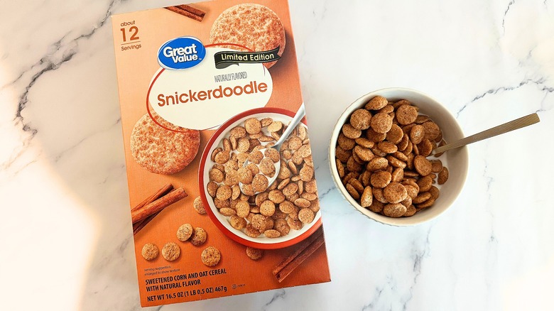 Box of Great Value Snickerdoodle cereal next to bowl of cereal with spoon on marble surface