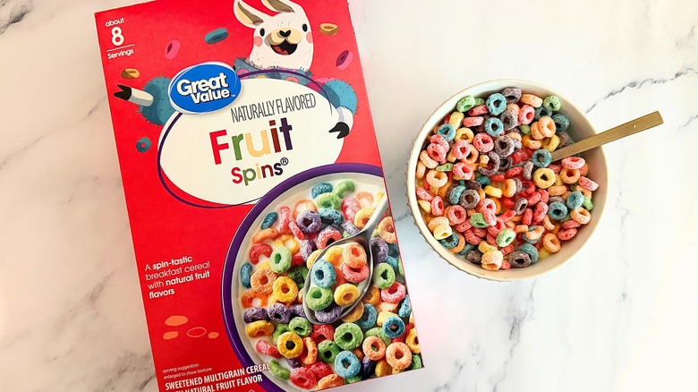 Box of Great Value Fruit Spins cereal next to bowl of cereal with spoon on marble surface