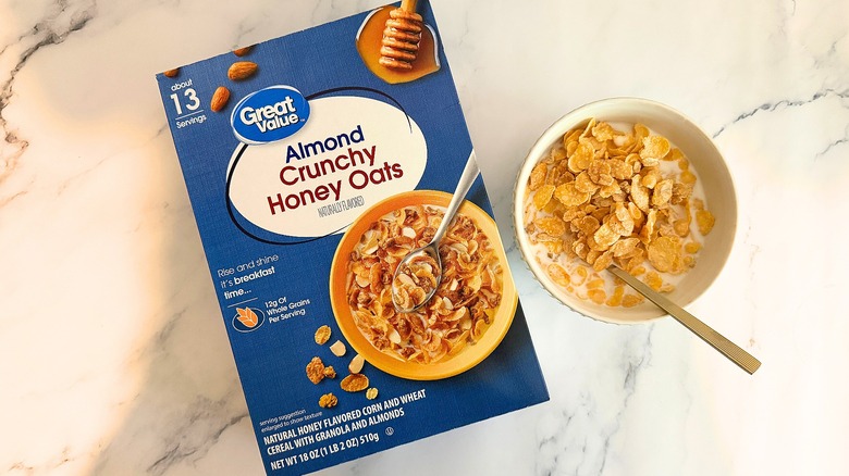 Box of Great Value Almond Crunchy Honey Oats cereal next to bowl of cereal with spoon on marble surface