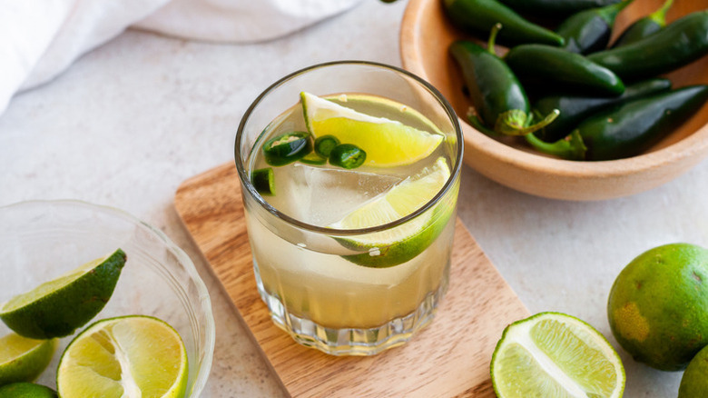 Spicy margarita cocktail in glass with ice cube, lime wedges, and jalapeno slices