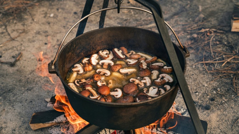 A cast iron pot full of mushrooms suspended over a fire
